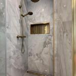 Dusche mit marblen Wänden und goldfarbenen Armaturen und Ablage