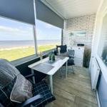 Terrasse mit Tisch, Stühlen und Meerblick. Weiße Wand mit Ziegeloptik und Fensterfront.