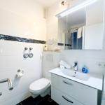 Badezimmer mit Dusche, Waschbecken und Toilette. Weiße Fliesen und Spiegelschrank.