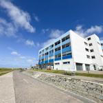 Moderne Wohnanlage mit blauen Balkonen und weißer Fassade an Strandpromenade.