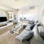 Wohnzimmer mit Sofa, Fernseher und Glas-Tisch. Fenster mit Blick nach draußen.