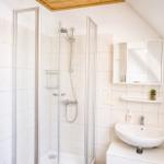 Badezimmer mit Dusche, Waschbecken und Spiegelschrank. Holzdecke und weiße Fliesen.