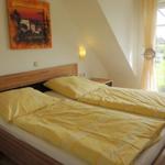 Zimmer mit Doppelbett, Holzgestell, Wandbild und Balkontür mit Blick auf Grünfläche.