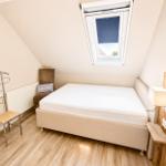 Schlafzimmer mit Dachschrägen, Bett, Fenster und Holzboden.