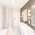 Badezimmer mit Dusche, Waschbecken und Toilette. Moderne Einrichtung mit Spiegel und Beleuchtung.