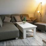Ein Wohnzimmer mit grauem Sofa, weißem Tisch und Holzwand.