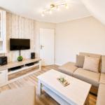 Wohnzimmer mit Sofa, Fernseher und Holzmöbeln. Dachschrägen und Lichtstrahler sorgen für Raumhöhe.