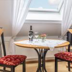 Runder Tisch mit zwei Stühlen unter Dachfenster. Tischdecke, Wein und Blumen.