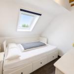 Schlafzimmer mit Dachfenster, weißem Bett und Holzwandverkleidung.
