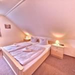 Schlafzimmer mit Doppelbett, zwei Nachttischen und Fenster mit Vorhängen.