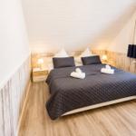 Schlafzimmer mit Doppelbett, Holzwand und Fenster mit Blick auf Dachziegel.