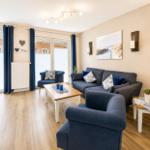 Wohnzimmer mit blauem Sofa, Sessel und Holztisch. Große Fenster mit blauen Vorhängen.