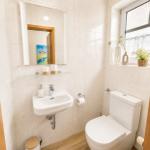 Badezimmer mit Toilette, Waschbecken und Spiegel. Fenster mit Pflanzen.