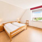 Schlafzimmer mit Doppelbett, zwei Nachttischen und Stuhl. Fenster mit Blick auf Garten.