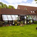Haus mit Glasveranda und Garten. Roter Ziegeldach, Pflanzen und Rasen.