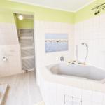 Badezimmer mit Badewanne, Dusche und Holzregal. Wandbild und grüne Farbe.