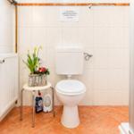 Badezimmer mit Toilette, kleinem Tisch und Blumen. Wand mit Hinweis und Heizkörper.