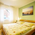 Schlafzimmer mit Doppelbett, grüner Wand und Fenster mit Vorhängen.