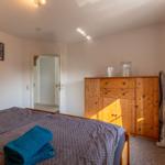 Schlafzimmer mit Bett, Holzschrank und Fenster. Auf dem Bett liegen gefaltete Handtücher.