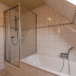 Badezimmer mit Dusche und Badewanne, belegt mit hellen Fliesen und Dachfenster.