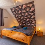 Schlafzimmer mit Holzbett, floraler Wandtapete und Nachttisch mit Lampe.
