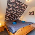 Schlafzimmer mit Holzbett, Blumenwand und Nachttisch mit Lampe.