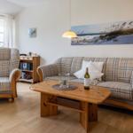 Wohnzimmer mit Sofa, Sessel und Holztisch. Wandbild zeigt Strand.