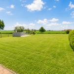 Großer grüner Garten mit Spielplatz und Grillhütte. Blick auf Felder und Himmel.