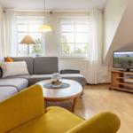 Wohnzimmer mit grauem Sofa, runden Tisch und Fernseher auf Holzstand.