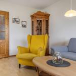 Wohnzimmer mit gelbem Sessel, grauem Sofa und Holztisch. Hintergrund: Holzschrank und Tür.