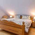 Schlafzimmer mit Holzbett, Nachttisch und Wickerstühlen unter schrägen Wänden.