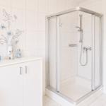 Badezimmer mit Dusche, Waschbecken und Schrank. Wandfliesen und Glasduschkabine.