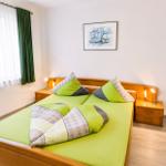 Schlafzimmer mit Doppelbett, grüner Bettwäsche, zwei Nachttischen und Fenster mit Vorhängen.