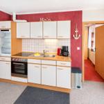 Küche mit weißen Schränken, Kühlschrank und Herd. Roter Wandverkleidung und Blick in den Flur.