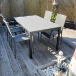 Terrasse mit Tisch und Stühlen, umgeben von Holzzaun und Steinbeeten.
