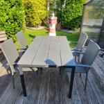 Terrasse mit Tisch und Stühlen, Blick auf Haus mit Solarpanelen und grünen Bäumen.