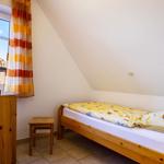 Ein Schlafzimmer mit Holzbett, Fenster und Schrank. Dachneigung und gestreifte Vorhänge.