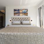 Schlafzimmer mit großem Bett, Wandbild und bodentiefen Fenstern.