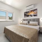 Schlafzimmer mit Bett, Nachttisch und Fenster. Wandbild und Klimaanlage sind sichtbar.