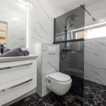 Bad mit Dusche, Waschbecken und Toilette. Fliesen und Spiegel sind sichtbar.