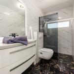 Badezimmer mit Dusche, Waschbecken und Toilette. Marmorwände und dunkler Boden.