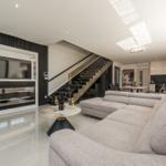 Großes Wohnzimmer mit Sofa, Glas-Treppe und Fernseher in moderner Einrichtung.