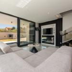 Großes Wohnzimmer mit Sofa, Fernseher und Blick auf Pool und Garten.