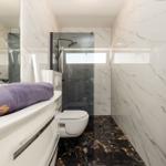 Badezimmer mit Marmorwänden, Dusche, Toilette und Waschtisch mit Handtuch.
