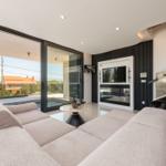 Großes Wohnzimmer mit Sofa, TV und Poolblick durch Glastüren.