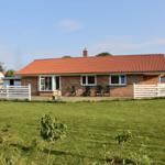 Ein Haus mit rotem Dach und weißer Umzäunung auf einer grünen Wiese.