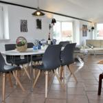 Essbereich mit Tisch und Stühlen, Wohnbereich mit Sofa und Fenstern.