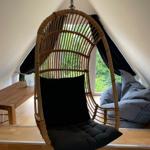Hängesessel aus Rattan mit schwarzer Polsterung im Dachbodenraum mit Fenster.