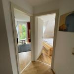 Hinter dem Flur sind Schlafzimmer und Wohnbereich mit Fenster und Holzboden sichtbar.