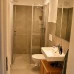 Badezimmer mit Dusche, WC und Waschbecken auf Holzschrank